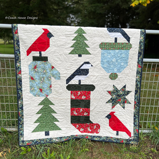 Quilt with winter-themed patterns including trees, birds, and a fire hydrant, displayed outdoors.