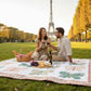 An image of a couple having a picnic in front of the Eiffel Tower. They are sitting on a butterfly patterned lap quilt in pinks and greens with a white background designed by Coach House Designs.