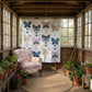 Sunroom with butterfly-patterned lap quilt hanging on wall with  armchair, and potted plants.