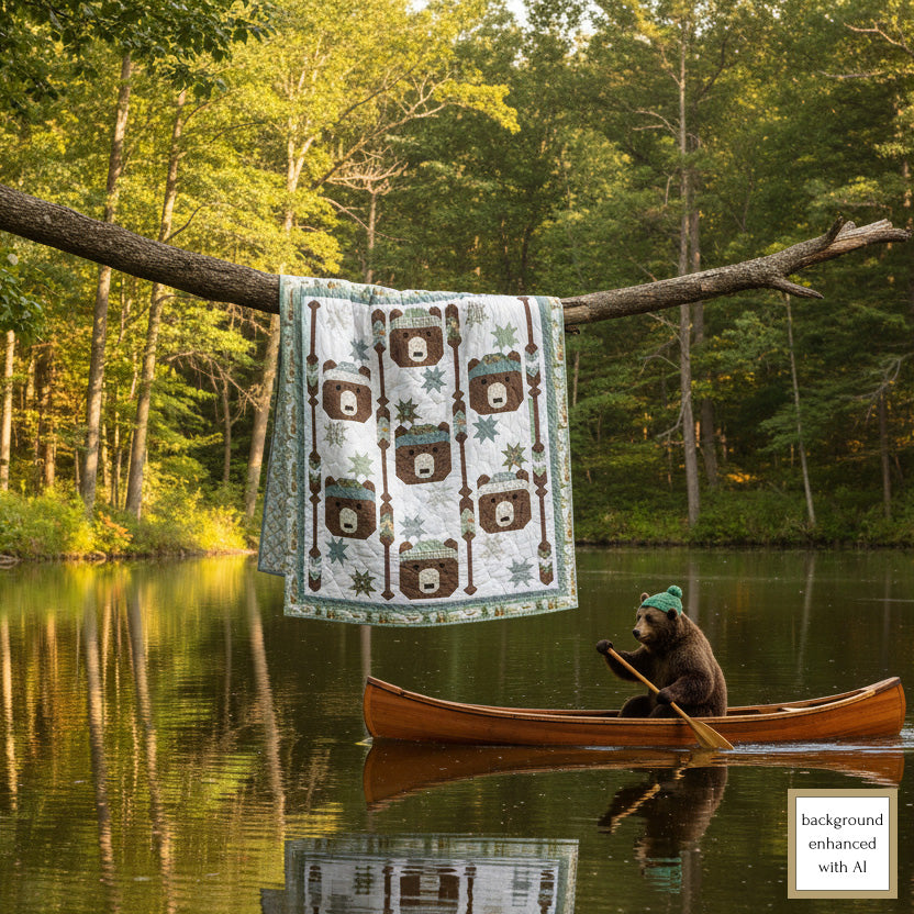 Lap quilt with bear pattern hanging on a tree branch over a lake with a bear in a canoe.